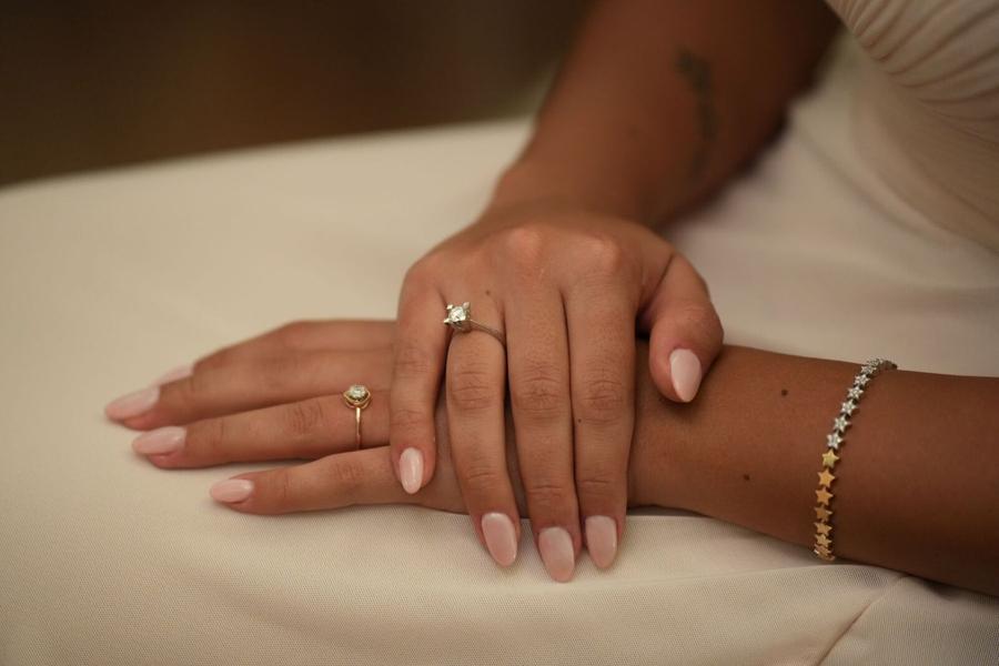 Soft nude nails on a hand wearing an engagement ring and a thin bracelet