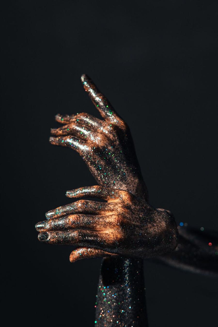 A hand dusted in metallic chrome pigment against a black backdrop