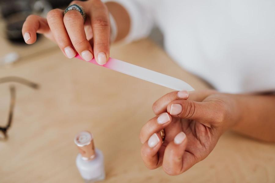 A technician shaping a client’s nails with a file