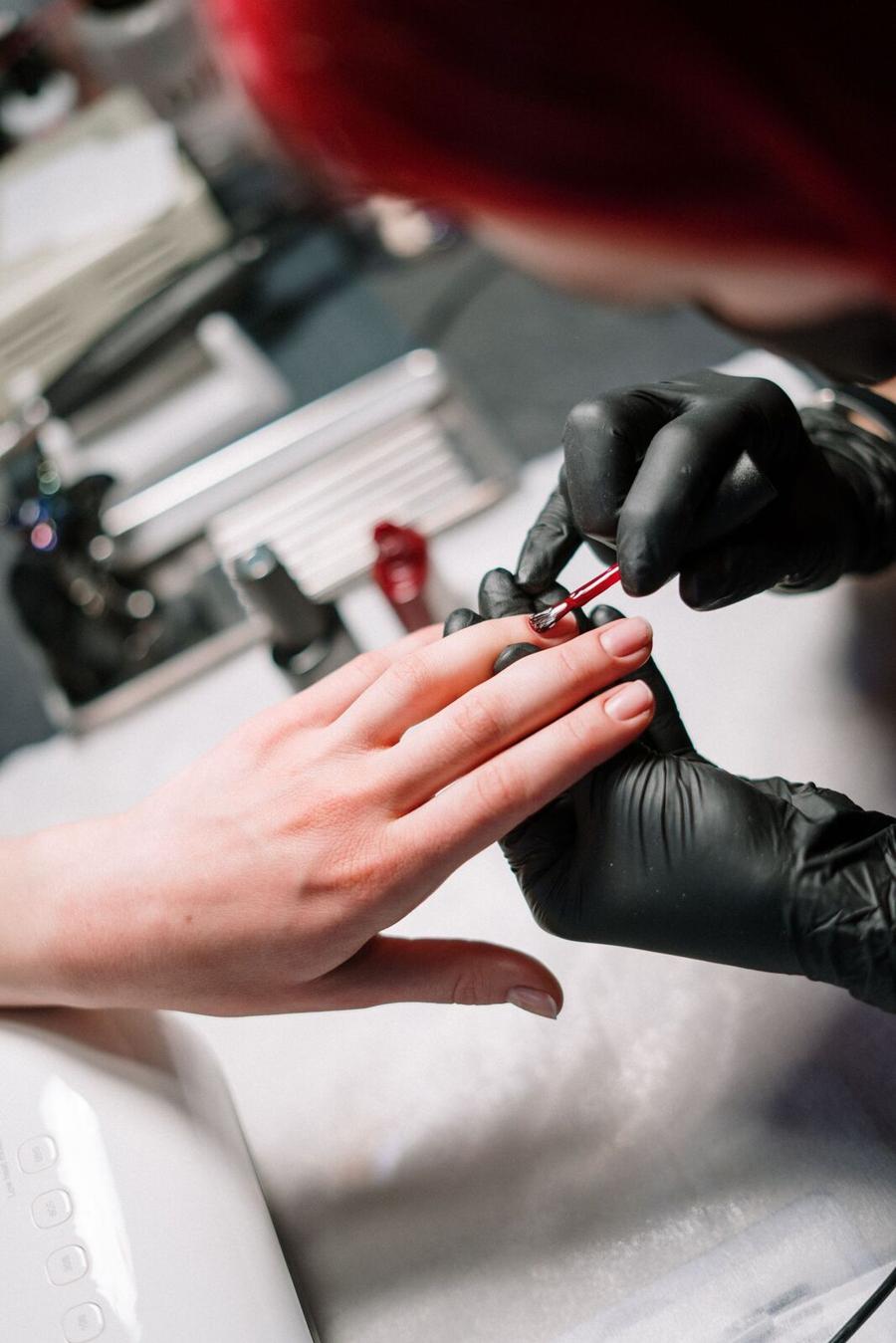 A nail technician painting a client’s nails under the desk lamp